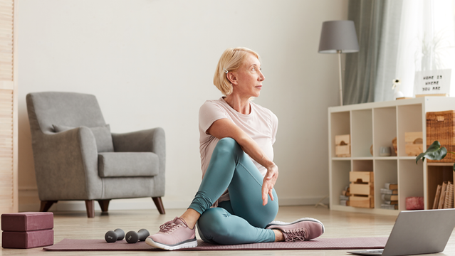 Frau sitzt auf der Yogamatte und folgt einem Online Kurs 